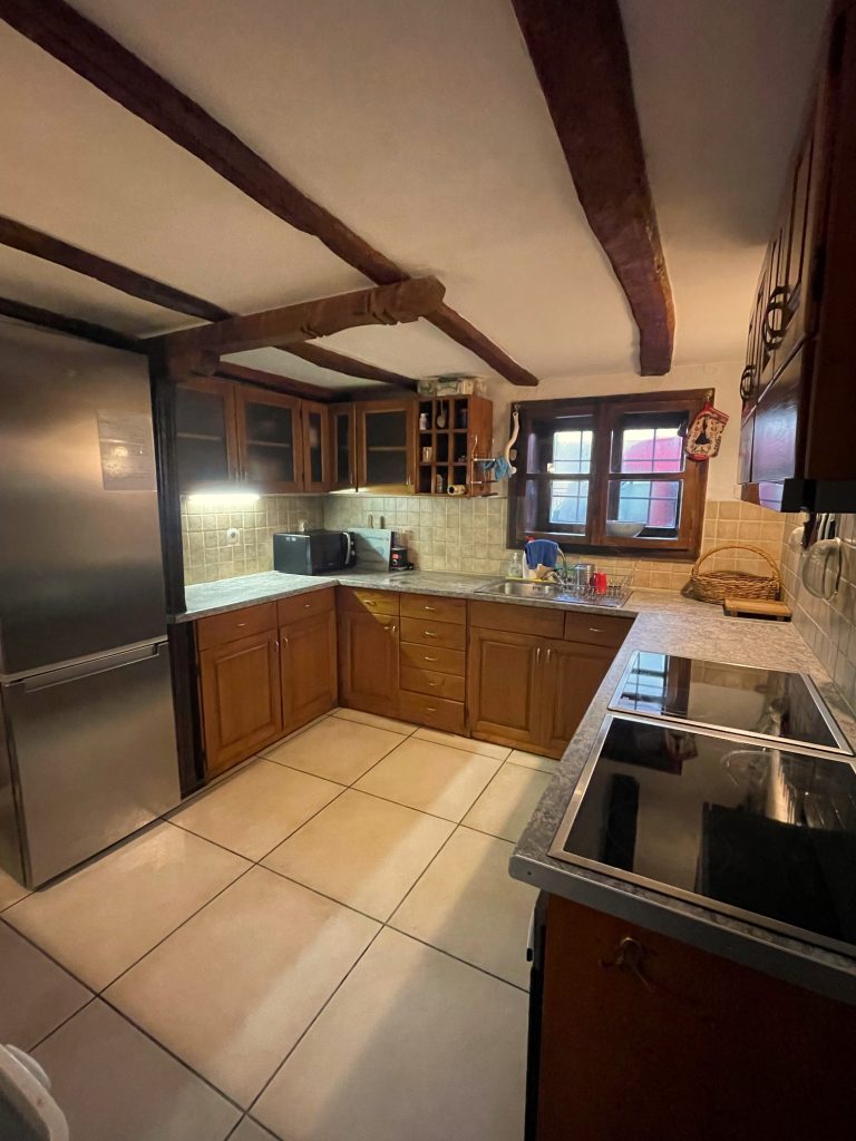 A kitchen with tiled floor and wooden cupboards. A window and fridge freezer can also be seen