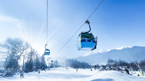 Bansko ski road covered in snow with the gondola above and people walking below. Snow on the peaks of the Pirin mountains.